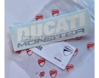 Puede incluir: Una pegatina Ducati Monster azul claro con letras blancas y borde plateado. La pegatina está sobre una bolsa de plástico transparente con logotipos Ducati rojos. También se ve una tarjeta blanca con un código de barras y el número 5003749228.
