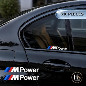 May include: Two M Power vinyl decals featuring the iconic blue, purple, and red slanted stripes followed by the white text M Power. These adhesive stickers are designed for application on car windows or body panels, shown here on a black vehicle.