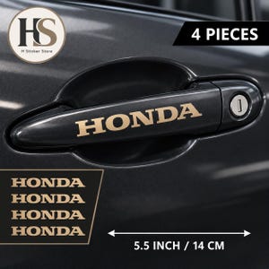 May include: A set of 4 beige Honda decals for a car door handle. Each sticker features the word HONDA in a bold, serif font. The decals measure 14 cm in length. The set includes four identical adhesive pieces for application on vehicle handles.