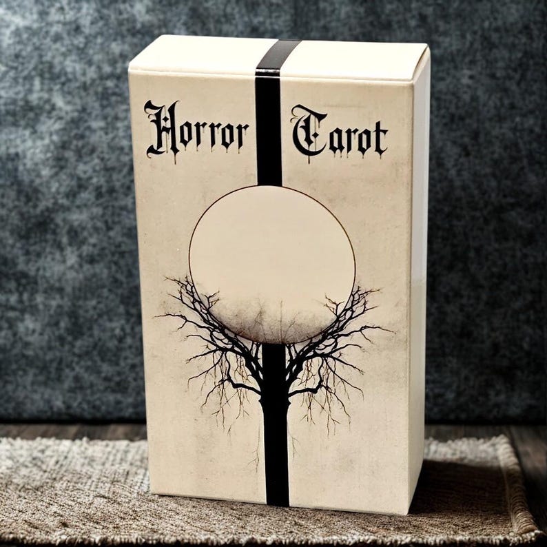 Peut inclure: Une bo&icirc;te de cartes de tarot beige avec les mots "Horror Tarot" en police gothique. Une bande noire verticale traverse le devant, croisant un cercle blanc avec une illustration d'arbre. La bo&icirc;te est sur une surface marron.