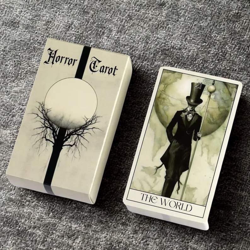 Peut inclure: Un jeu de cartes de tarot et une carte avec une illustration gothique. La bo&icirc;te du jeu est blanc cass&eacute; avec les mots "Horror Tarot" et une bande noire. La carte montre une figure en haut-de-forme et les mots "The World".