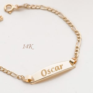 Könnte beinhalten: Ein goldfarbenes Armband mit einem Namensschild mit der Aufschrift "Oscar". Das Armband hat ein Kettenglied-Design und einen Verschluss. Der Text "14K" ist ebenfalls sichtbar.