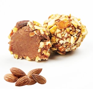 May include: Two chocolate truffles coated in chopped almonds, one cut open to reveal the creamy interior. A small pile of whole almonds is in the foreground. The truffles are a delicious treat.