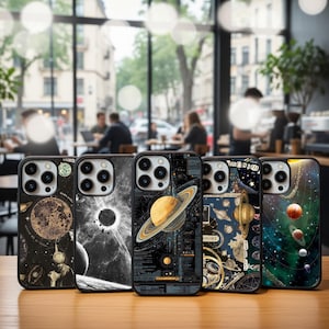 May include: Five phone cases with space-themed designs are displayed on a wooden table. The cases feature planets, stars, and celestial bodies in various colors. The cases are black with a camera cutout.