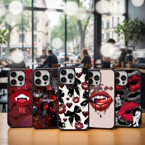 Könnte beinhalten: Eine Sammlung von fünf Handyhüllen mit verschiedenen Designs. Die Hüllen zeigen Bilder von roten Lippen, Herzen, Schleifen und den Texten "Bite Me" und "Vampier". Die Hüllen sind schwarz und haben eine glänzende Oberfläche.