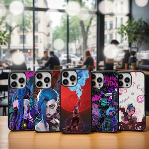 May include: Five smartphone cases with distinctive designs are arranged on a wooden surface. The cases showcase vibrant illustrations of a blue-haired character, a red moon, and graffiti-style text. The cases have black borders and are likely for a smartphone.