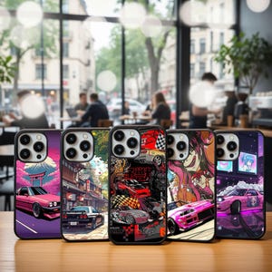 May include: A collection of five phone cases with vibrant, colorful designs. Each case features a unique graphic, including anime-style illustrations and images of cars. The cases are displayed on a wooden surface, with a blurred cafe background.