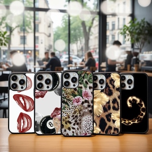 Peut inclure: Présentation de cinq coques de téléphone avec des motifs variés. Les coques présentent des imprimés de lèvres rouges, une boule de billard noire, un imprimé léopard avec des fleurs, des fleurs dorées et une spirale léopard. Elles sont exposées sur une surface en bois.