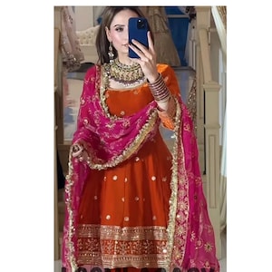 Peut inclure: Ensemble salwar kameez orange et fuchsia avec broderies et ornements dorés. Un dupatta fuchsia assorti avec une bordure dorée drape les épaules. Le texte "LOOMLAGACY" est visible.