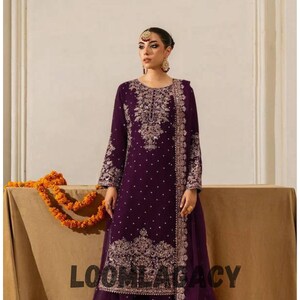 May include: A plum-coloured, embroidered formal outfit. The long-sleeved top and matching skirt feature intricate gold-coloured embroidery. The outfit includes a sheer scarf and is displayed on a neutral background. The text "LOOMLEGACY" is visible.