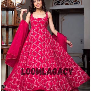 May include: A vibrant red dress with a white floral pattern and matching scarf. The dress has a square neckline and a flowing skirt. The text "LOOMLAGACY" is printed across the bottom of the dress. This elegant outfit is suitable for special occasions.