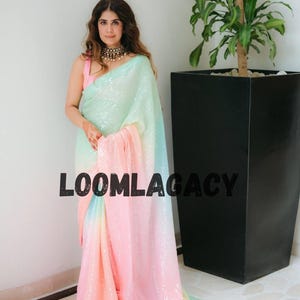 Puede incluir: Una mujer con un sari de lentejuelas en tonos pastel. El sari hace una transición de verde menta a azul y luego a rosa. El texto "LOOMLAGACY" está impreso en el sari. La mujer lleva un top rosa y un collar dorado.