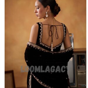 May include: A dark brown velvet sari with intricate gold embroidery. The sari features a low-cut back and a matching shawl. The text "LOOMLAGAC" is visible on the sari. The woman is wearing gold earrings and a necklace.