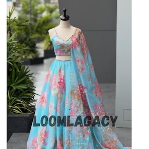 May include: A light blue floral print lehenga choli set. The set includes a top, skirt, and a matching dupatta. The floral pattern features pink and peach flowers. The text "LOOMLAGACY" is visible at the bottom of the image.