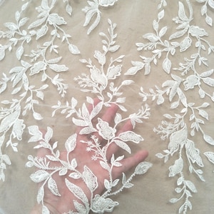 Può includere: Tessuto di pizzo ricamato floreale bianco. Il design delicato presenta foglie e fiori dettagliati. Il pizzo è su uno sfondo trasparente di colore chiaro, creando una bella trama. Ideale per abiti da sposa, abiti o progetti artigianali.