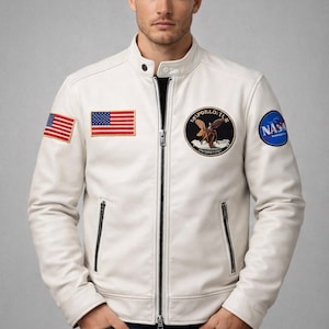 May include: Cream-colored leather jacket with a stand-up collar, zipper closure, and multiple patches. Features an American flag patch, a NASA patch, and an Apollo 11 patch. The jacket has two zippered pockets and is worn with dark blue jeans.