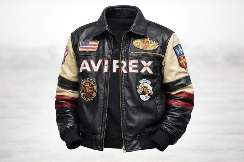 May include: A black leather jacket featuring the text AVIREX across the chest, a front zipper, and multiple colorful embroidered patches. The sleeves are accented with beige and red stripes, and the cuffs and hem are finished with black ribbed knit.