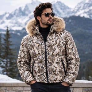 Op de afbeelding: Een gewatteerd jack met een bruin en beige slangenprint, een zwarte ritssluiting aan de voorzijde en een capuchon afgezet met dikke, pluizige bruine imitatiebont. Het jack wordt gedragen over een zwarte coltrui en een donkere broek.