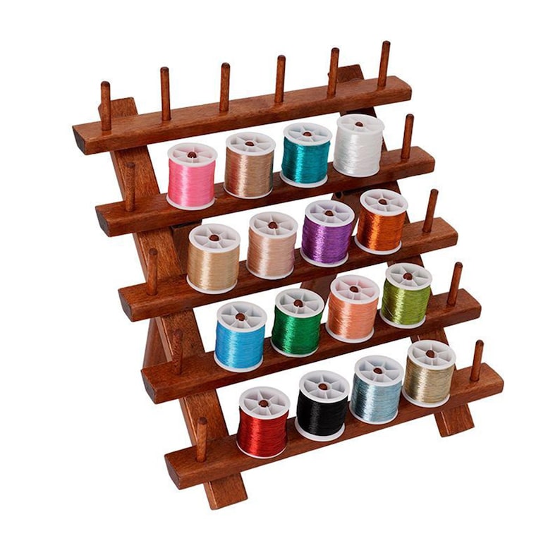 May include: A wooden thread spool organizer with multiple levels, holding colorful spools of thread. The spools are in various colors, including pink, teal, white, gold, and purple. The organizer is made of dark wood and has a tiered design.