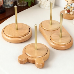 Puede incluir: Cuatro soportes de madera para carretes de hilo con varillas de latón. Los soportes tienen varias formas, incluyendo redondas y ovaladas, y tienen un acabado de madera natural. Las varillas de latón se extienden hacia arriba desde el centro de cada soporte.