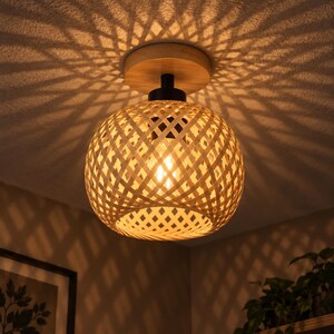 May include: A spherical ceiling light fixture featuring a woven bamboo shade with a natural light brown finish. The lamp is mounted to the ceiling with a circular wooden base and a black metal connector, casting intricate geometric shadows.