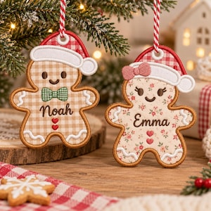 May include: Two embroidered gingerbread person ornaments hanging by red and white striped strings. One features a tan gingham pattern, a green bowtie, and the name Noah. The other has a floral pattern, a pink bow, and the name Emma.