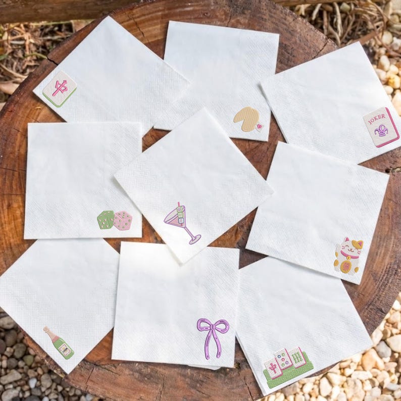 May include: A set of eight white square paper napkins, each featuring a small, distinct colorful illustration in the corner. Designs include a mahjong tile, a fortune cookie, a joker card, two dice, a martini glass, a lucky cat, a bottle, and a bow.