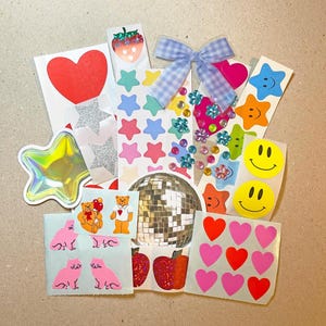 May include: A collection of colorful stickers featuring various designs. Includes a red heart, glitter stars, smiley faces, star shapes, a disco ball, and a gingham bow. Also includes stickers of cats, bears, and strawberries.