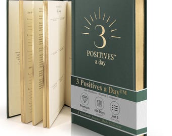 May include: A dark green hardcover journal with gold foil lettering on the cover reading 3 POSITIVES a day. The journal features gold-edged pages and a paper belly band with the text 3 Positives a Day, Premium Design, 366 Days, and Just 3 Lines a Day.