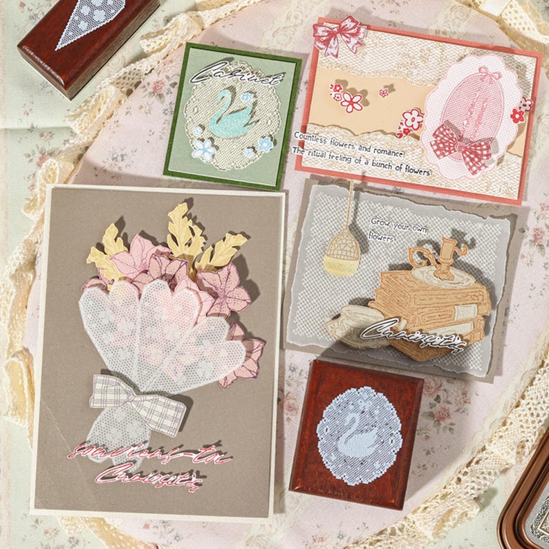 May include: A collection of handmade greeting cards and wooden stamps featuring lace textures, floral motifs, and swan illustrations. The cards include text such as Countless flowers and romance, The ritual feeling of a bunch of flowers, and Grow your own flowers.