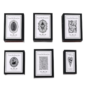 May include: Six rectangular black boxes with white labels featuring the text Evening Wind Weaving Yarn and A ETERNAL SILENCE. The labels display black and white illustrations of candles, a flower, lace, a swan, stars, and a heart shape.