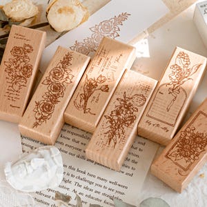May include: A set of six rectangular wooden stamps featuring detailed brown ink illustrations of various flowers including roses, tulips, and lilies of the valley, along with vintage-style postal markings and handwritten script text.