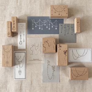 May include: A collection of rectangular wooden rubber stamps featuring intricate designs of hanging chains, stars, ribbons, and floral motifs, accompanied by several paper samples displaying the stamped impressions in black and blue ink.