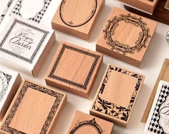 May include: A collection of wooden stamps with various decorative border designs. Some stamps feature oval, square, and floral frames. One stamp reads "Whispers in the Border". The stamps are arranged on a white surface.