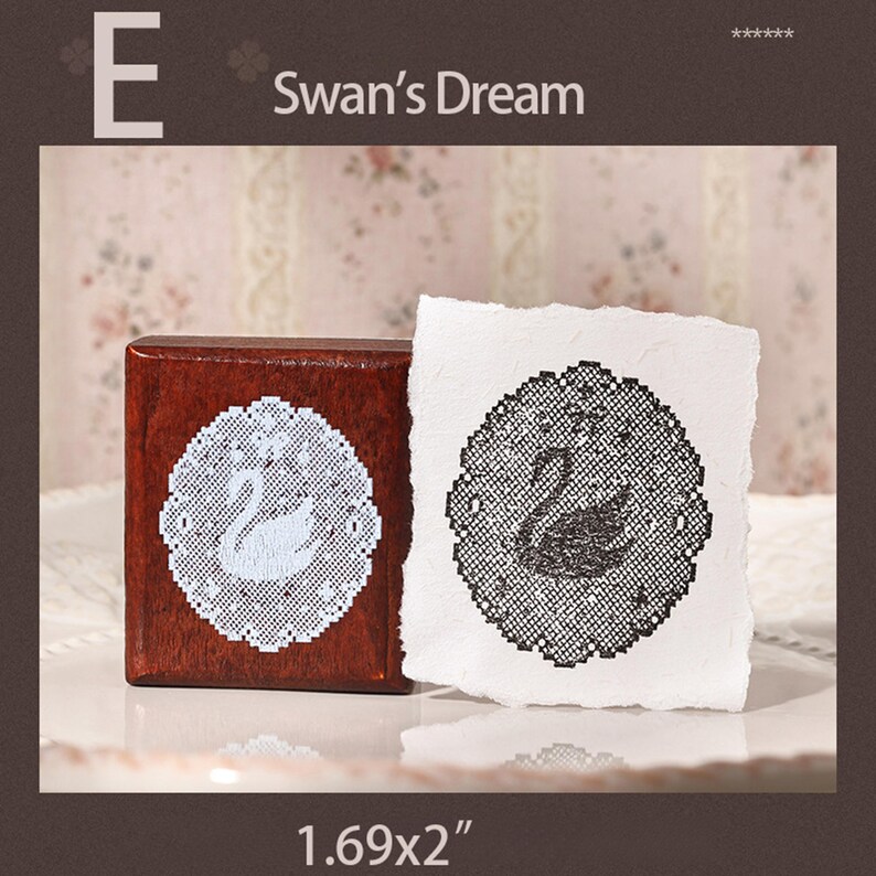 May include: A square wooden stamp featuring a white lace-style swan design, accompanied by a white paper square showing a black ink impression of the same swan motif. The text E Swan's Dream and the dimensions 1.69x2 inches are visible.