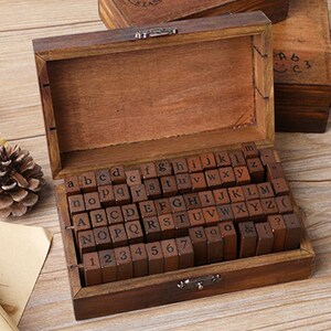 May include: A wooden box with a hinged lid, filled with individual wooden letter stamps. The stamps include the alphabet, numbers, and symbols. The box is a dark brown color and has a metal clasp.