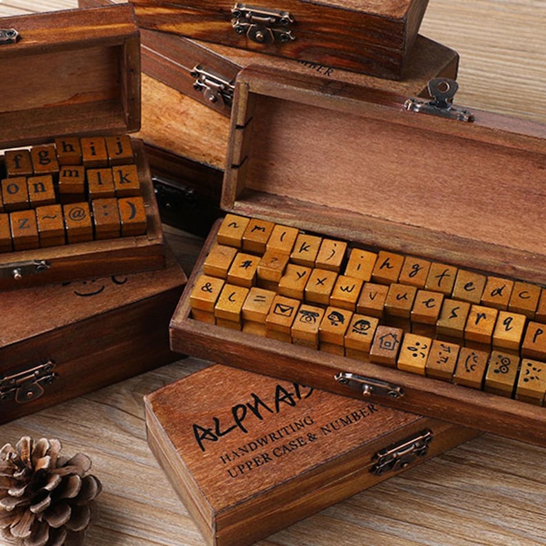 May include: Wooden alphabet stamp sets with individual letter blocks arranged in open boxes. The boxes are brown with metal clasps. One box is labeled "ALPHAL HANDWRITING UPPER CASE & NUMBER".