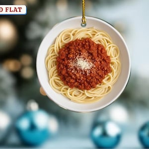 May include: A round, white ornament featuring a bowl of spaghetti with meat sauce and a sprinkle of parmesan cheese. The ornament has a gold string for hanging and the text "2D FLAT" in a blue box.