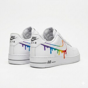 以下が含まれることがあります： 白いナイキエアフォース1スニーカー。側面に虹色のドリップデザイン、かかとにナイキエアのブランドロゴ。靴底に黒いストライプが入っています。