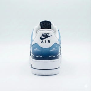 Puede incluir: Zapatillas Nike Air Force 1 blancas y azules con un dise&ntilde;o personalizado. El tal&oacute;n presenta el logotipo de Nike y "AIR" en negro. El dise&ntilde;o incluye un paisaje marino con nubes, olas y p&aacute;jaros. La suela es blanca.