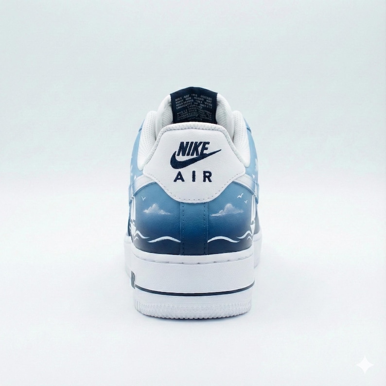 Puede incluir: Zapatillas Nike Air Force 1 blancas y azules con un dise&ntilde;o personalizado. El tal&oacute;n presenta el logotipo de Nike y "AIR" en negro. El dise&ntilde;o incluye un paisaje marino con nubes, olas y p&aacute;jaros. La suela es blanca.