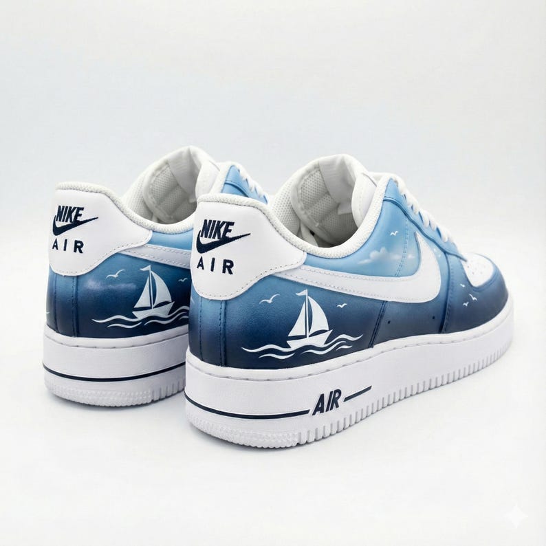 Puede incluir: Un par de zapatillas blancas y azules con tem&aacute;tica n&aacute;utica. Los zapatos presentan un dise&ntilde;o azul degradado con un velero y p&aacute;jaros. El logotipo de Nike es visible en el tal&oacute;n.