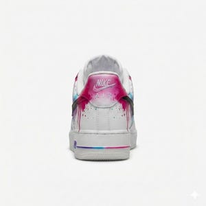 May include: White Nike Air Force 1 sneakers with a colorful paint drip design on the heel and sides. The heel features the Nike Air logo in pink. The sole has a gradient of pink, blue, and purple.