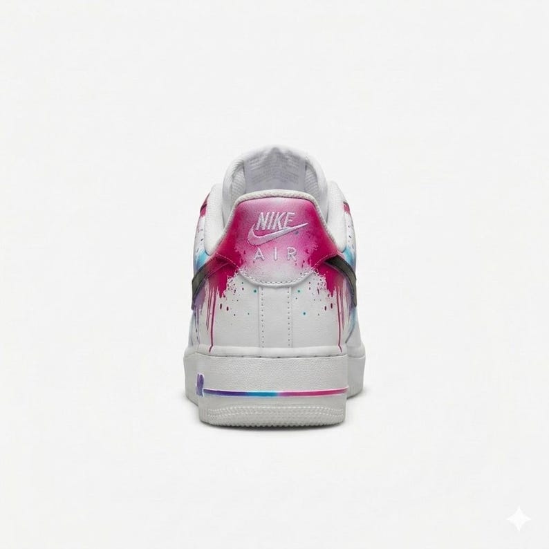May include: White Nike Air Force 1 sneakers with a colorful paint drip design on the heel and sides. The heel features the Nike Air logo in pink. The sole has a gradient of pink, blue, and purple.