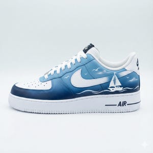 Puede incluir: Zapatilla Air Force 1 blanca y azul con dise&ntilde;o n&aacute;utico. La zapatilla presenta una suela blanca, un logo Nike blanco y una parte superior azul degradada con un gr&aacute;fico de velero y la palabra "AIR".