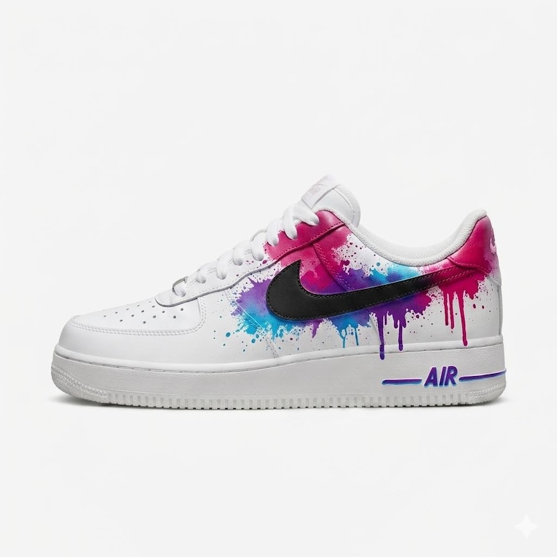 May include: White leather sneaker with a colorful paint splatter design in pink, blue, and purple. Features a black swoosh logo and the word "AIR" in blue. A stylish and artistic footwear choice.