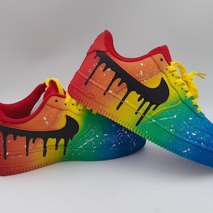 Pode incluir: Um par de t&eacute;nis personalizados com um design de gradiente arco-&iacute;ris. Os sapatos fazem a transi&ccedil;&atilde;o do vermelho para o azul, com atacadores amarelos e pingos pretos. Salpicos brancos adicionam detalhes. O log&oacute;tipo da Nike &eacute; preto.