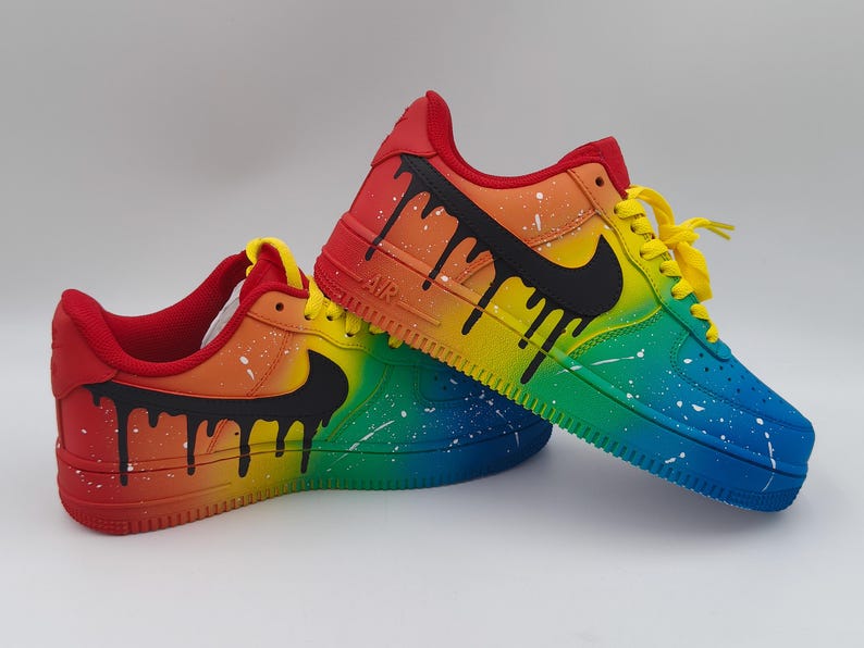 Pode incluir: Um par de t&eacute;nis personalizados com um design de gradiente arco-&iacute;ris. Os sapatos fazem a transi&ccedil;&atilde;o do vermelho para o azul, com atacadores amarelos e pingos pretos. Salpicos brancos adicionam detalhes. O log&oacute;tipo da Nike &eacute; preto.