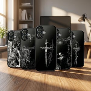 May include: A collection of black phone cases with white graphic designs. The cases feature various gothic-inspired illustrations, including a sword, architectural elements, and abstract patterns. The cases are displayed on a wooden surface.