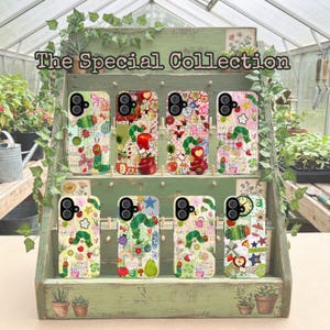 May include: A display of phone cases with colorful, whimsical designs. The cases feature illustrations of a caterpillar, apples, and patchwork patterns. The text "The Special Collection" is at the top. The cases are arranged on a green wooden shelf with potted plants.
